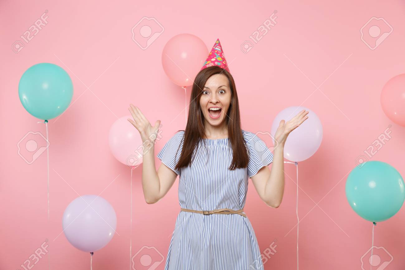 Portrait of fascinating young happy woman in birthday hat and blue dress spreading hands on bright trending pink background with colorful air baloons. Birthday holiday party, people sincere emotions - 108168205 Portrait of fascinating young happy woman in birthday hat and blue dress spreading hands on bright trending pink background with colorful air baloons. Birthday holiday party, people sincere emotions - 108168205