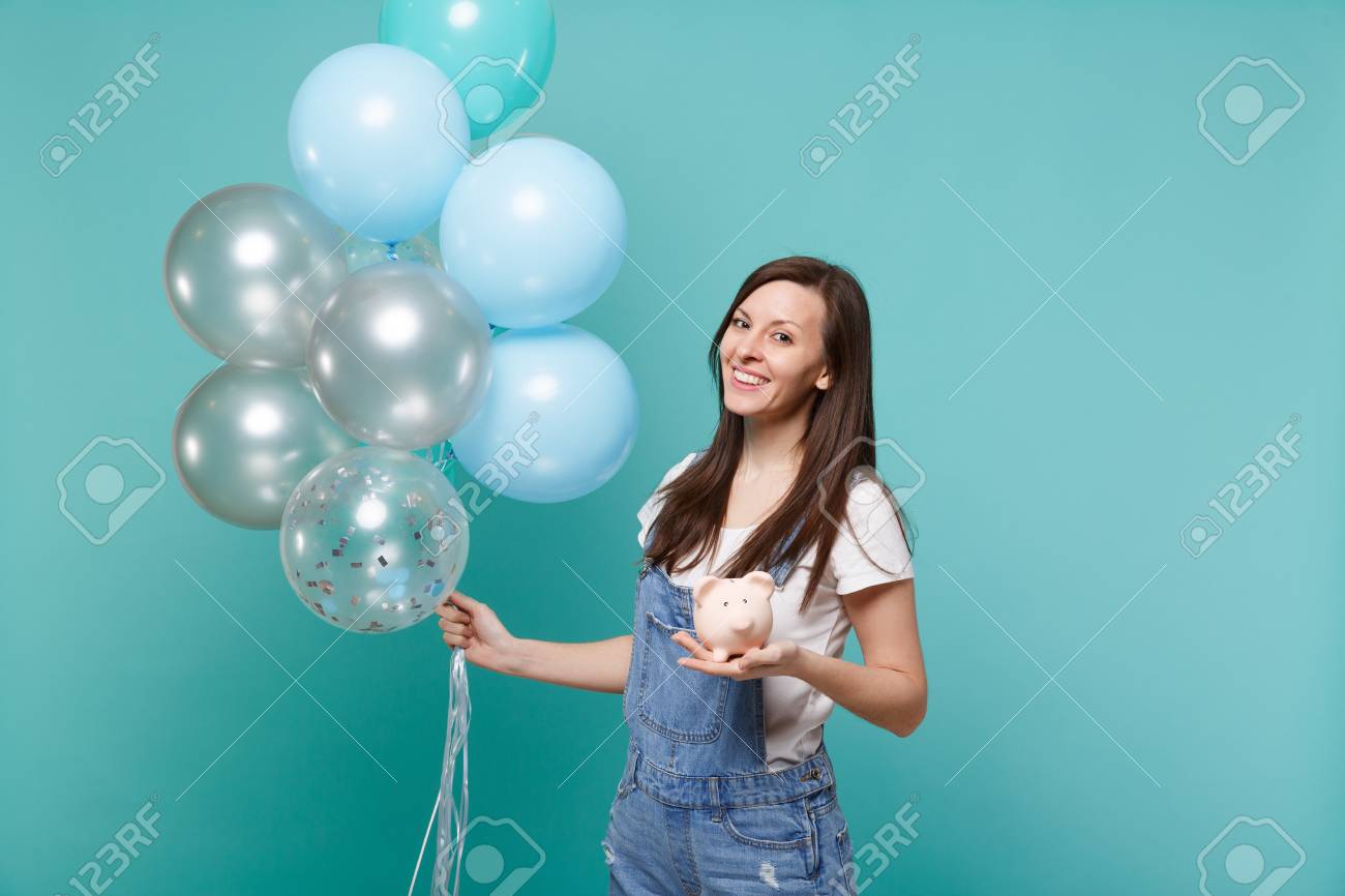Portrait of smiling young woman in denim clothes holding piggy money bank celebrating with colorful air balloons isolated on blue turquoise background. Birthday holiday party, people emotions concept - 116188778 Portrait of smiling young woman in denim clothes holding piggy money bank celebrating with colorful air balloons isolated on blue turquoise background. Birthday holiday party, people emotions concept - 116188778