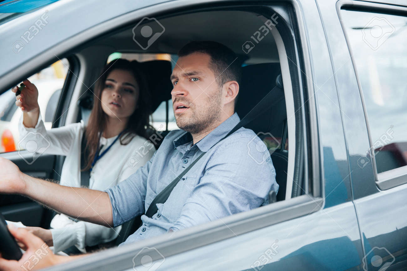 Female instructor showing something by his hand on the road and giving advice. Male student listening to his teacher, looking ahead with concentration and holding wheel. Driving school concept. - 157808617 Female instructor showing something by his hand on the road and giving advice. Male student listening to his teacher, looking ahead with concentration and holding wheel. Driving school concept. - 157808617