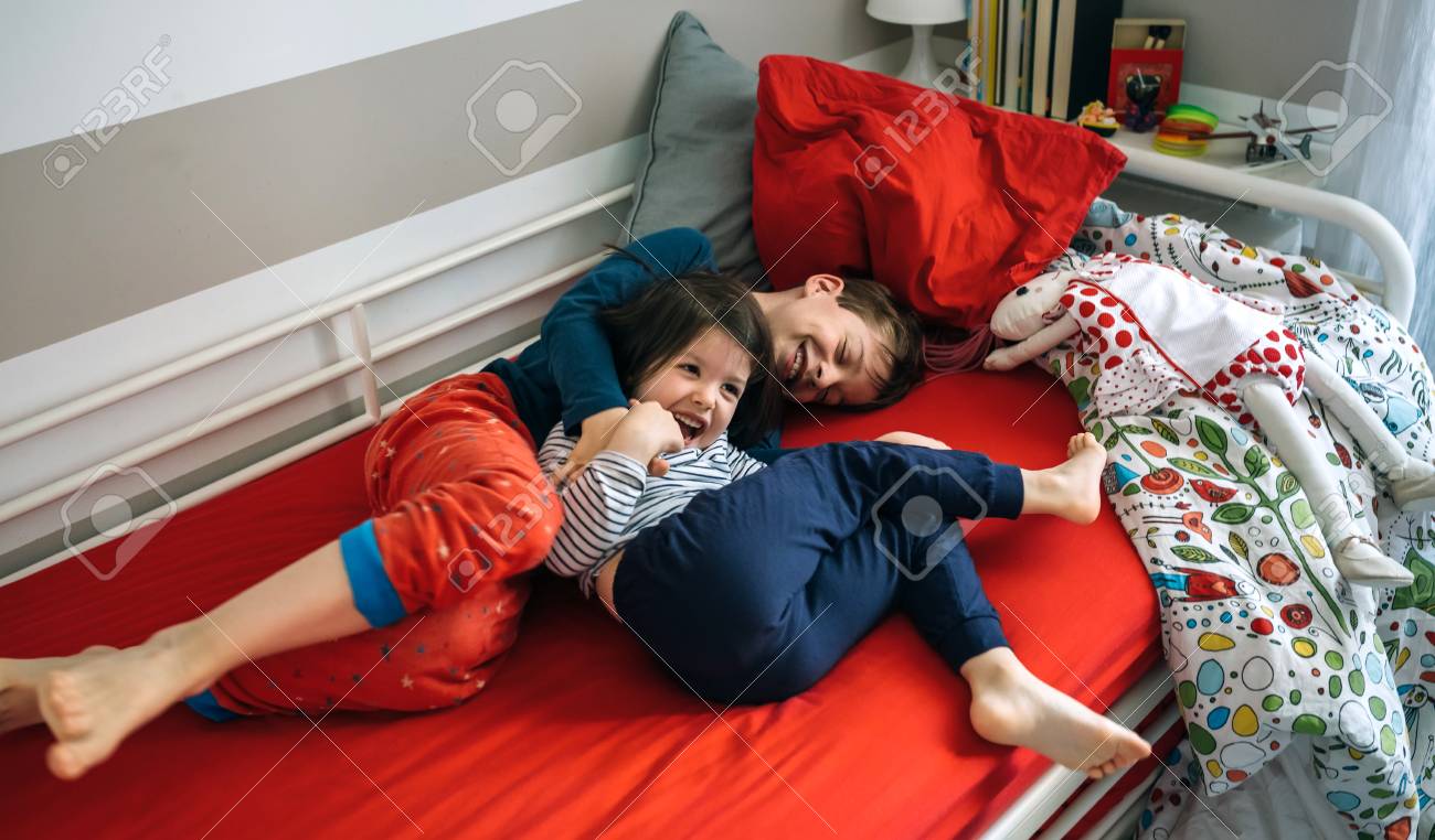 Brother and sister tickling and laughing while lying on the bed - 100403216 Brother and sister tickling and laughing while lying on the bed - 100403216