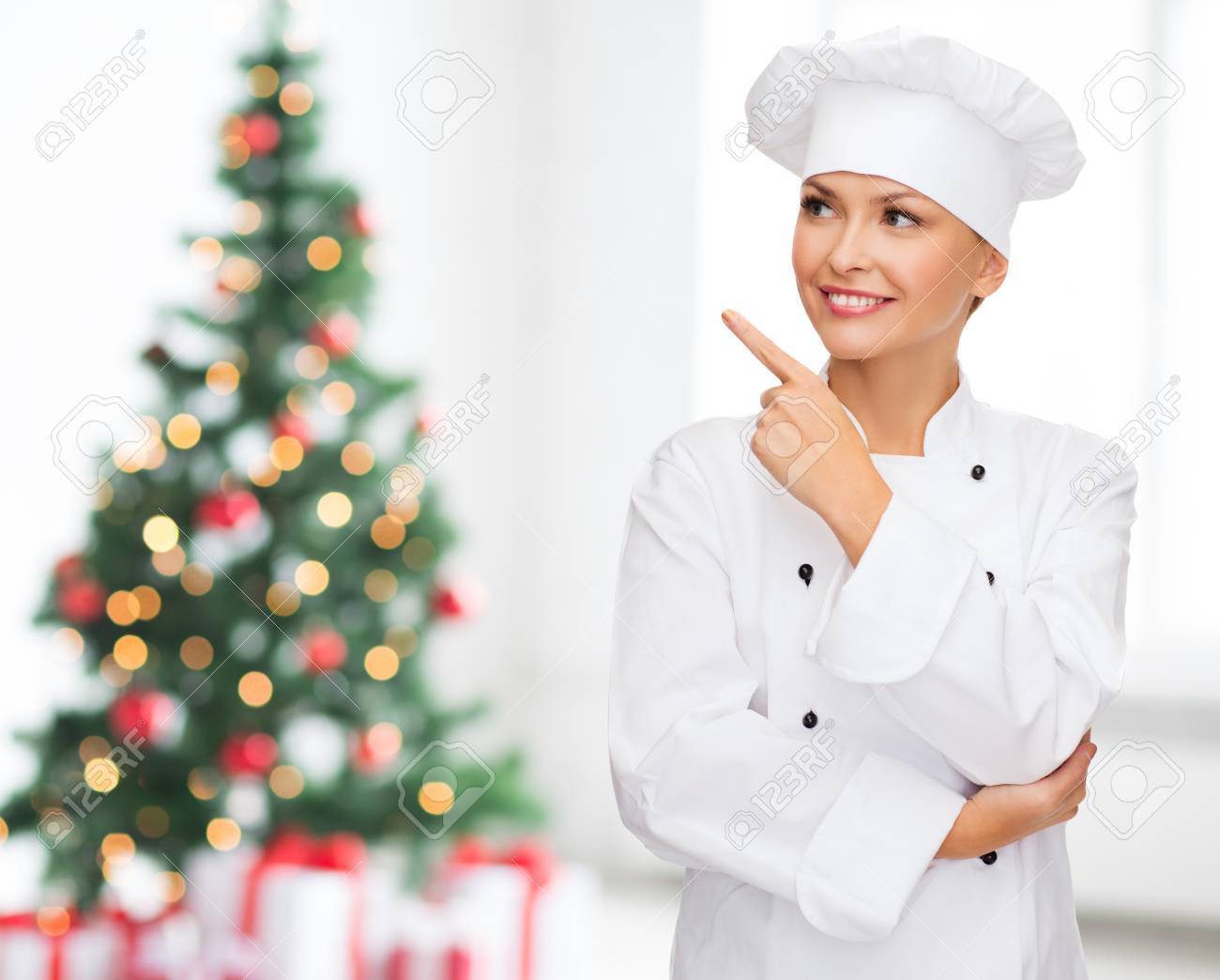 女性シェフ 料理やパン屋リビング ルームとクリスマス ツリーの背景の上を指を指して笑って料理 休日および人々 コンセプト の写真素材 画像素材 Image