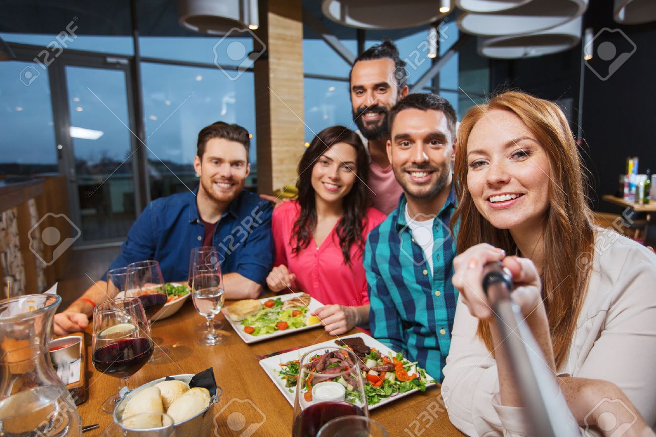 leisure, technology, friendship, people and holidays concept - happy friends having dinner and taking picture by selfie stick at restaurant - 53241227 leisure, technology, friendship, people and holidays concept - happy friends having dinner and taking picture by selfie stick at restaurant - 53241227