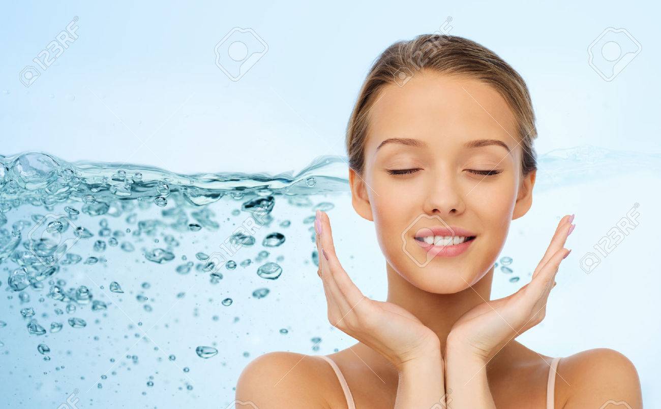 beauty, people, skincare and health concept - smiling young woman face and hands over water splash on blue background - 53315896 beauty, people, skincare and health concept - smiling young woman face and hands over water splash on blue background - 53315896