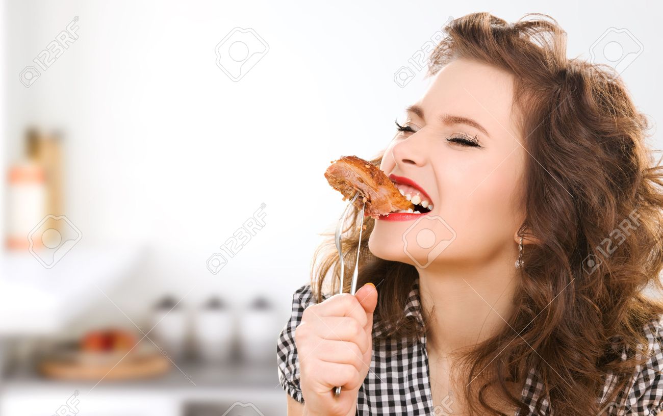 people, diet, culinary and food concept - hungry young woman eating meat on fork over kitchen background - 53725849 people, diet, culinary and food concept - hungry young woman eating meat on fork over kitchen background - 53725849