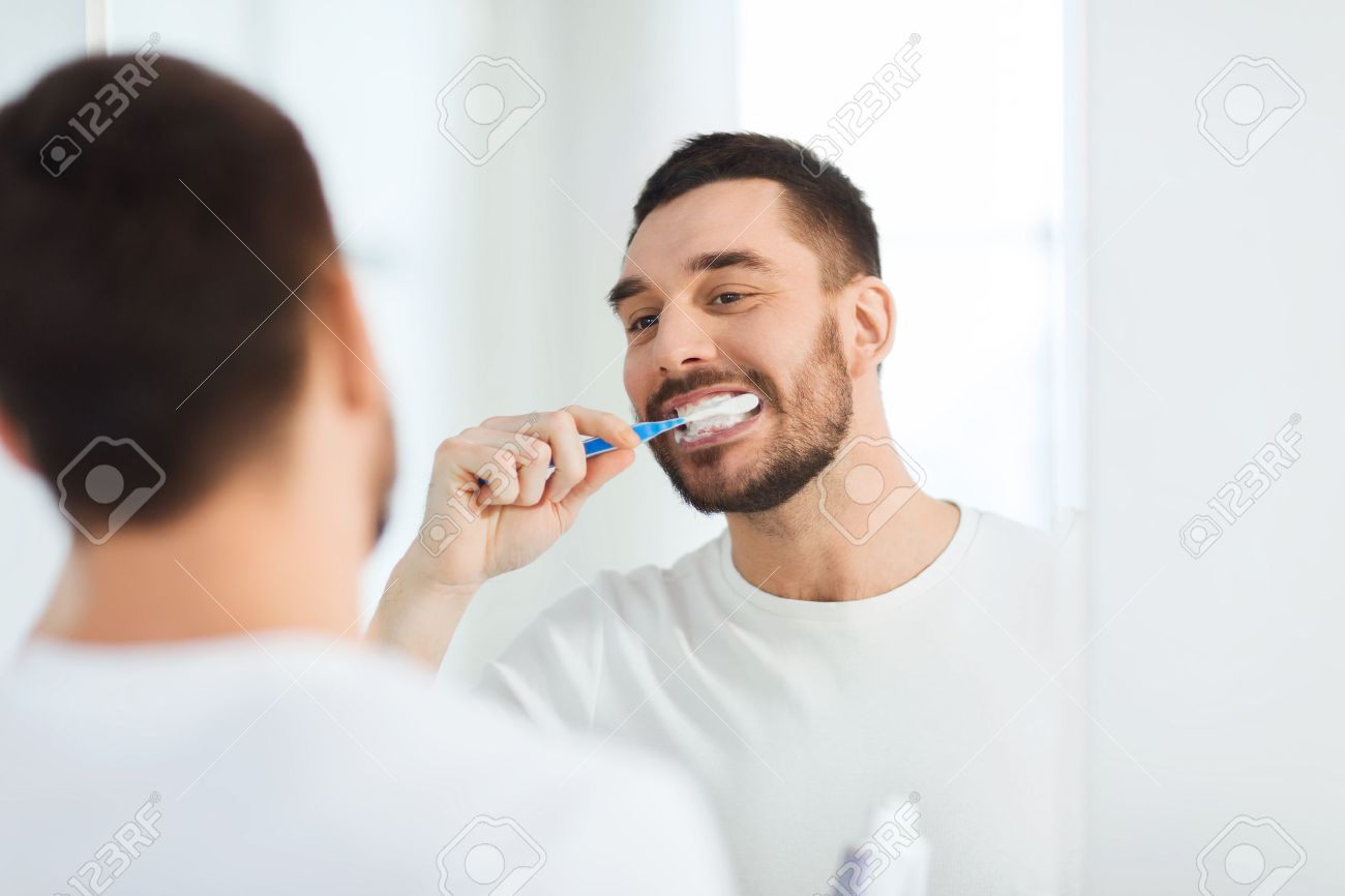health care, dental hygiene, people and beauty concept - smiling young man with toothbrush cleaning teeth and looking to mirror at home bathroom - 54867700 health care, dental hygiene, people and beauty concept - smiling young man with toothbrush cleaning teeth and looking to mirror at home bathroom - 54867700