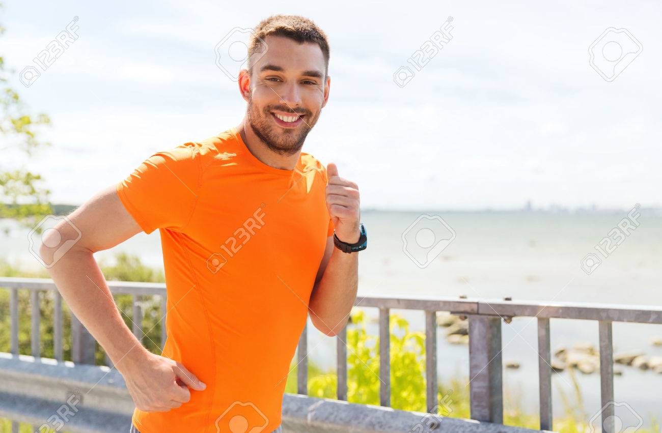 fitness, sport, people, technology and healthy lifestyle concept - smiling young man with heart rate watch running at summer seaside - 54776693 fitness, sport, people, technology and healthy lifestyle concept - smiling young man with heart rate watch running at summer seaside - 54776693