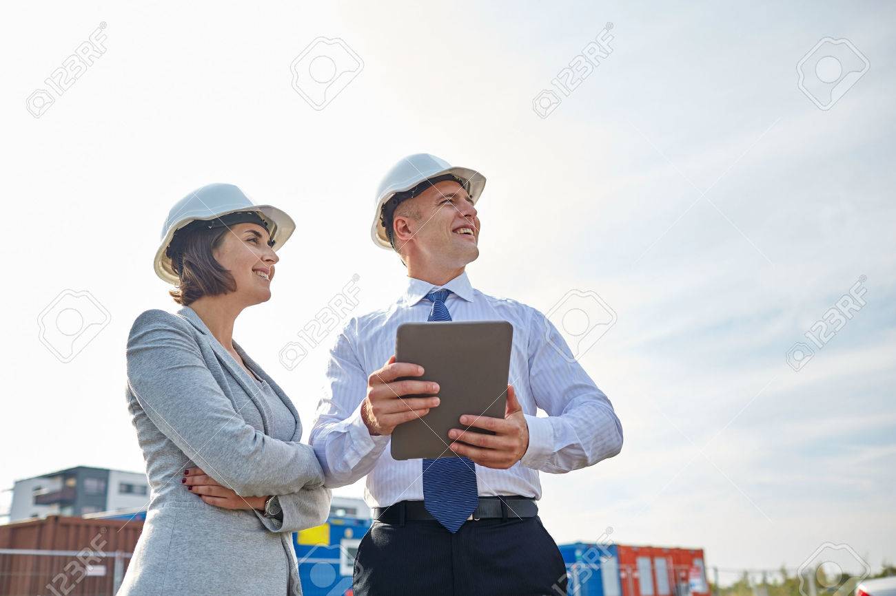 smiling man and woman in hardhats with tablet pc computer at construction site - 57668069 smiling man and woman in hardhats with tablet pc computer at construction site - 57668069