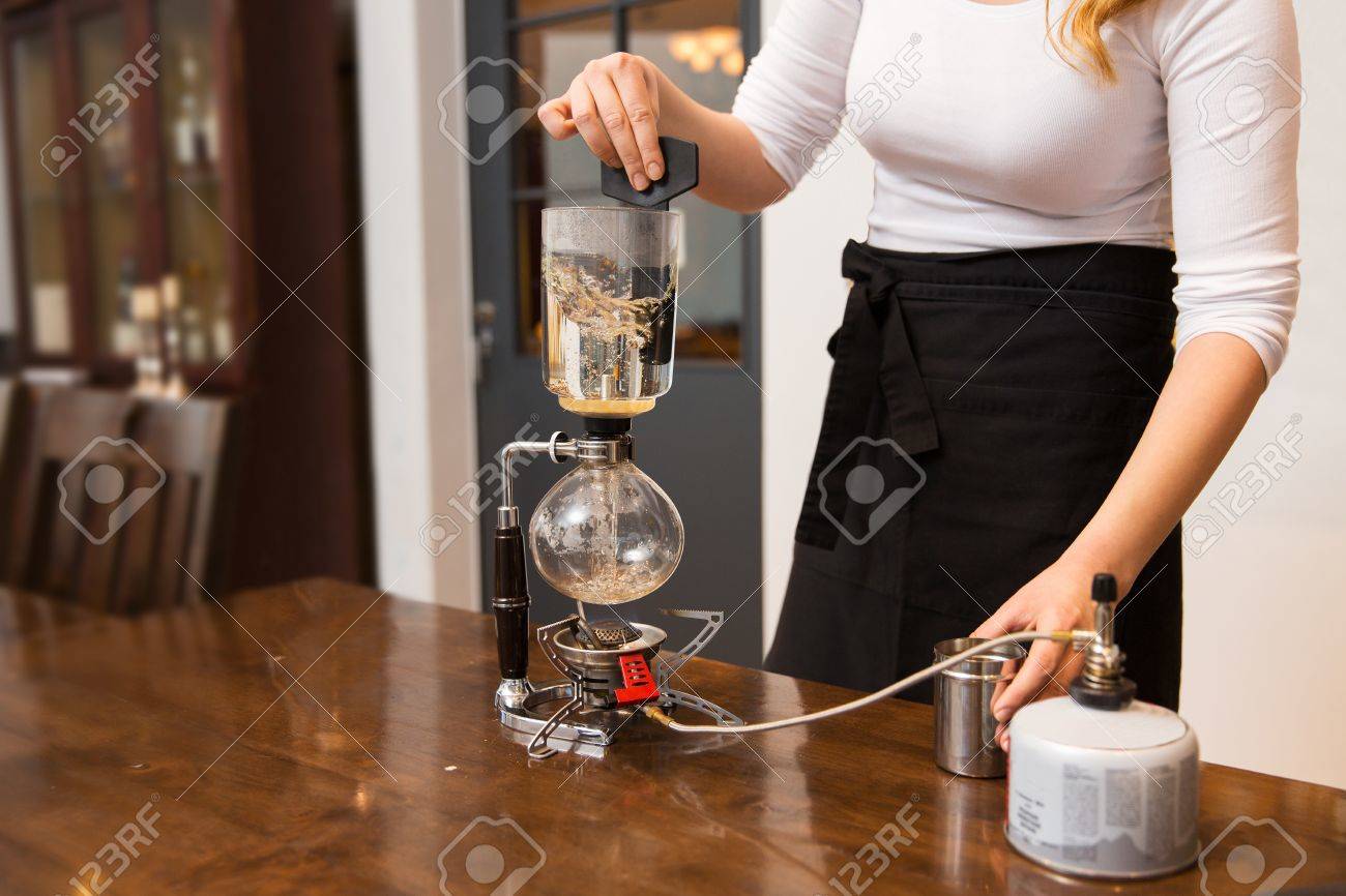 Equipos, cafetería, la gente y la tecnología concepto cerca de la mujer con agua de calefacción con quemador de gas butano en la cafetera sifón en Equipos, cafetería, la gente y la tecnología concepto cerca de la mujer con agua de calefacción con quemador de gas butano en la cafetera sifón en