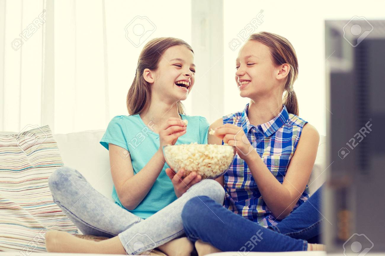 二人の幸せな少女はテレビを見て 笑って ポップコーンを家で食べる の写真素材 画像素材 Image