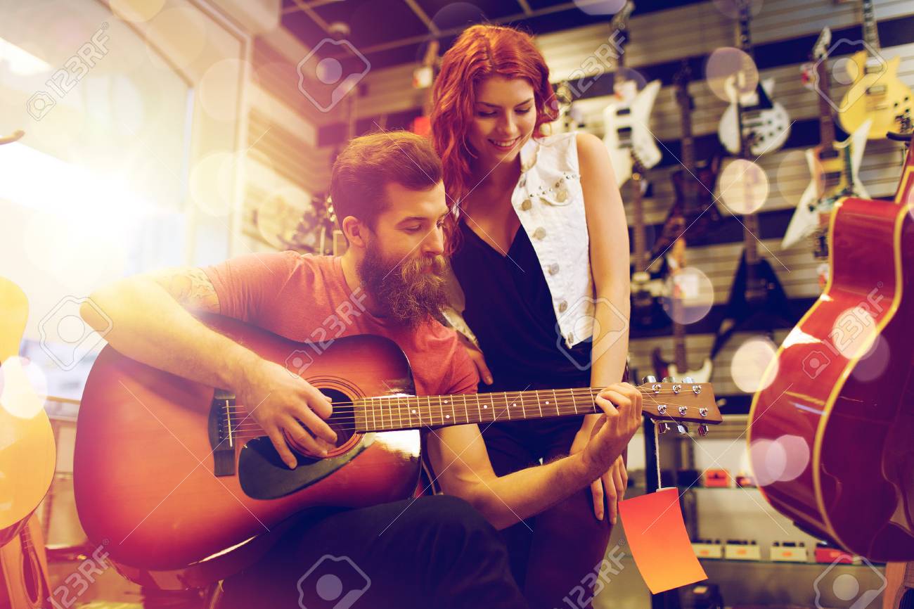 Concepto De Personas E Instrumentos Musicales - Feliz Pareja De Músicos Tocando La Guitarra En La Tienda De Música Sobre Luces Fotos, Retratos, Imágenes Y Fotografía De Archivo Libres De Derecho.