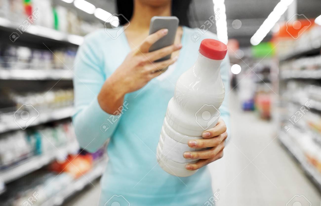 woman with smartphone buying milk at supermarket - 103677363 woman with smartphone buying milk at supermarket - 103677363