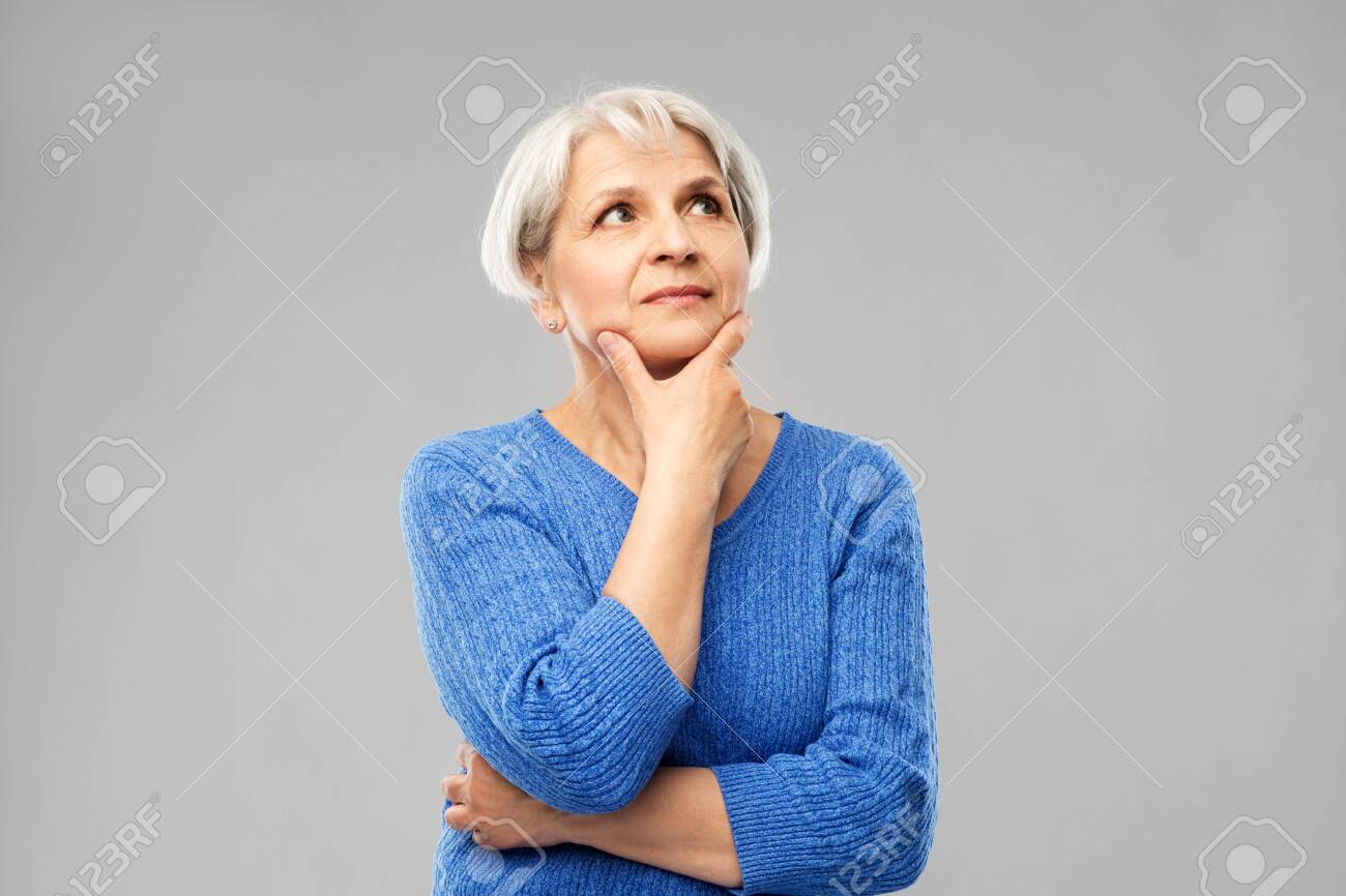 Old people and decision making concept - portrait of senior woman in blue sweater thinking over grey background - 122308265 Old people and decision making concept - portrait of senior woman in blue sweater thinking over grey background - 122308265