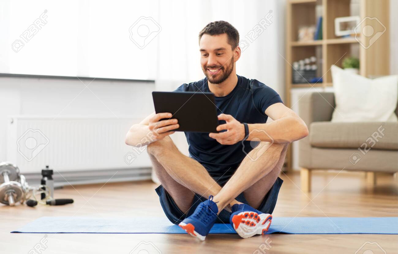 Man with tablet computer on exercise mat at home - 123603161 Man with tablet computer on exercise mat at home - 123603161