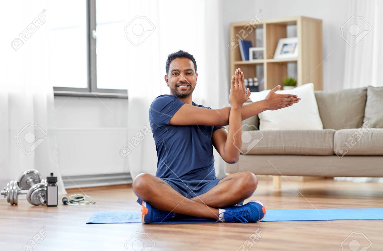 sport, fitness and healthy lifestyle concept - indian man training and stretching arm at home - 125557709 sport, fitness and healthy lifestyle concept - indian man training and stretching arm at home - 125557709