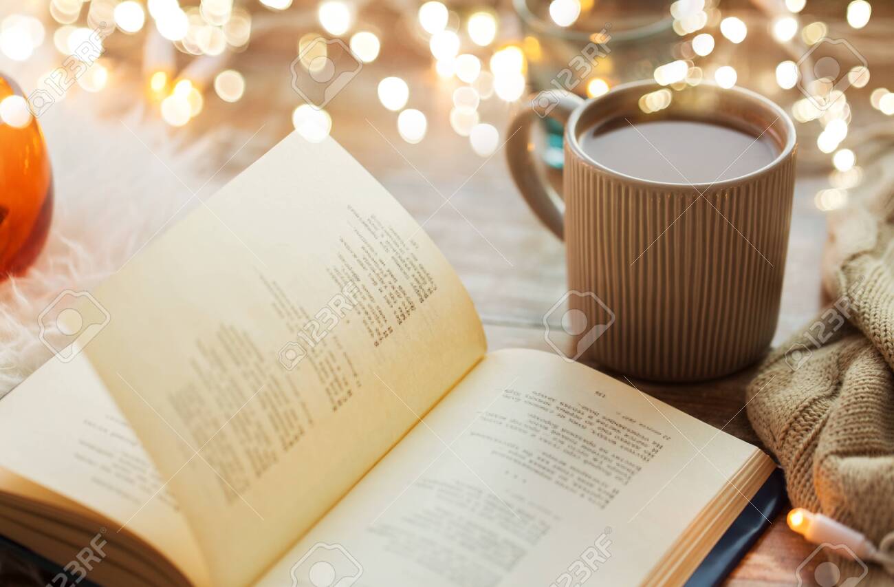 hygge and cozy home concept - book and cup of coffee or hot chocolate on table - 130120813 hygge and cozy home concept - book and cup of coffee or hot chocolate on table - 130120813