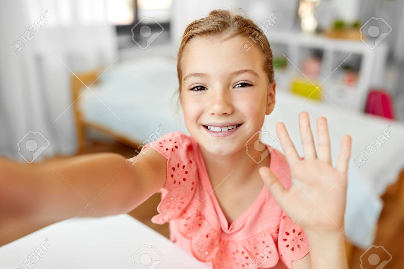 happy girl taking selfie and waving hand at home - 130746212 happy girl taking selfie and waving hand at home - 130746212