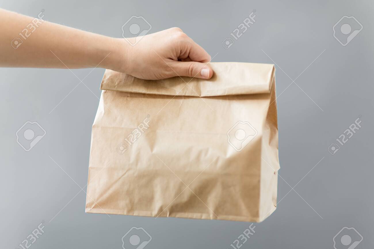 recycling and ecology concept - hand holding disposable brown takeaway food in paper bag with lunch on table - 135399171 recycling and ecology concept - hand holding disposable brown takeaway food in paper bag with lunch on table - 135399171