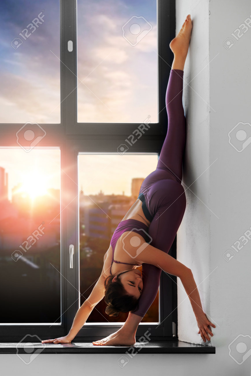woman doing yoga exercise on window sill at studio - 169910220 woman doing yoga exercise on window sill at studio - 169910220