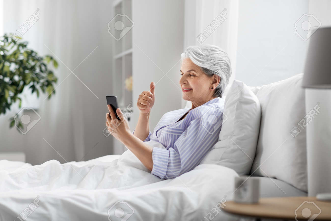 senior woman with phone having video call in bed - 169967844 senior woman with phone having video call in bed - 169967844