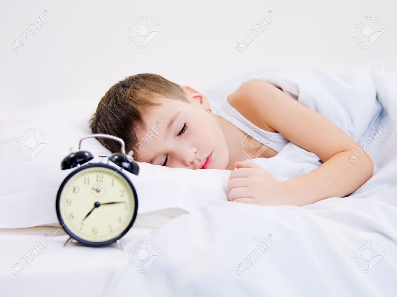 sweet kid sleeping with alarm clock near his head stock photo