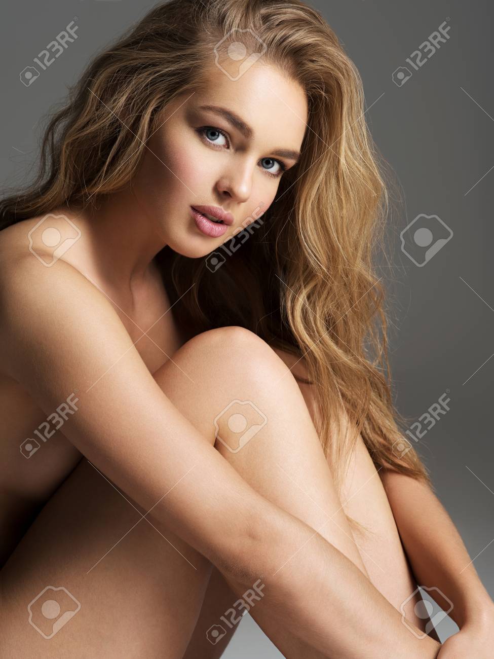 Linda Jovem Mulher Nua Senta-se No Estúdio. Linda Mulher Com Corpo Nu. Belo  Retrato De Uma Menina Loira Com Longo Cabelo Encaracolado. Foto Royalty  Free, Gravuras, Imagens e Banco de fotografias. Image