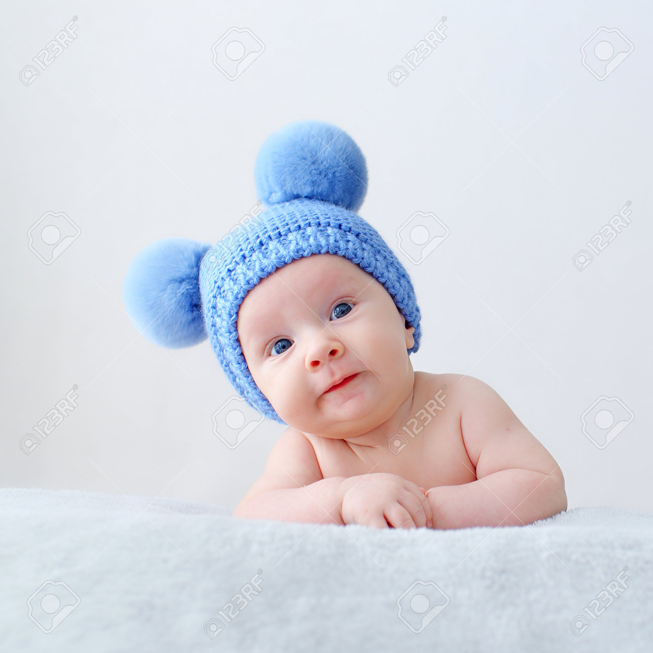 Sweet Newborn Baby In A Blue Hat With Pompoms Looks Into The Camera. Fun  Beautiful, Cute Little Infant With Blue Eyes Looks Into The Camera. A Calm  Two-month-old Kid Is Lying On, image size:1300x1300
