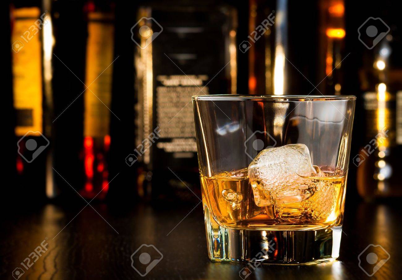 whiskey glass with ice in front of bottles on wood table - 28755714 whiskey glass with ice in front of bottles on wood table - 28755714