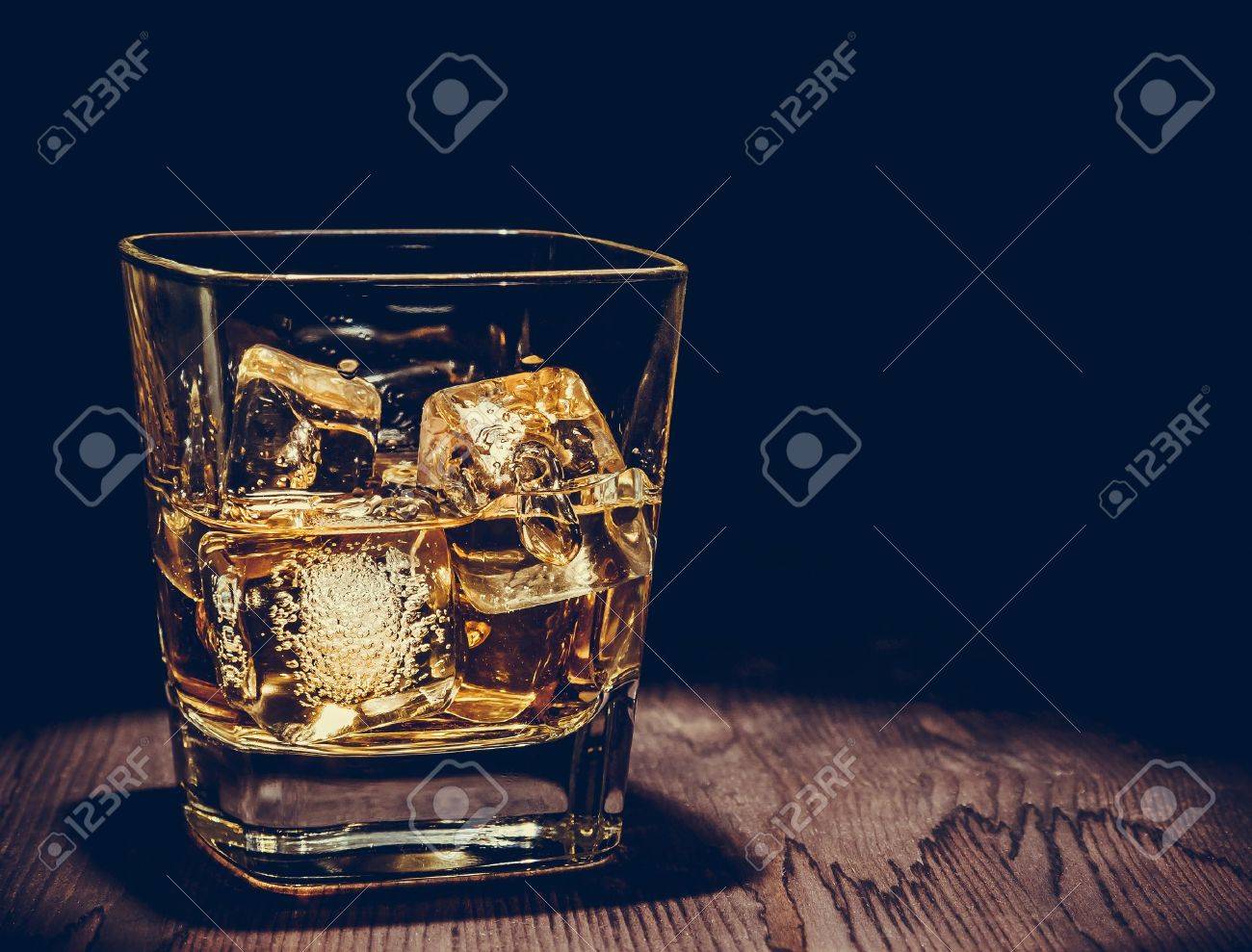 glass of whiskey with ice cubes on wood table, warm atmosphere, time of relax with whisky with space for text - 46673642 glass of whiskey with ice cubes on wood table, warm atmosphere, time of relax with whisky with space for text - 46673642