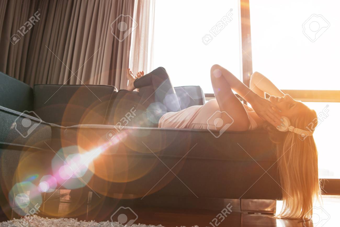 woman listening to music with sun flare coming from window of apartment - 80699608 woman listening to music with sun flare coming from window of apartment - 80699608