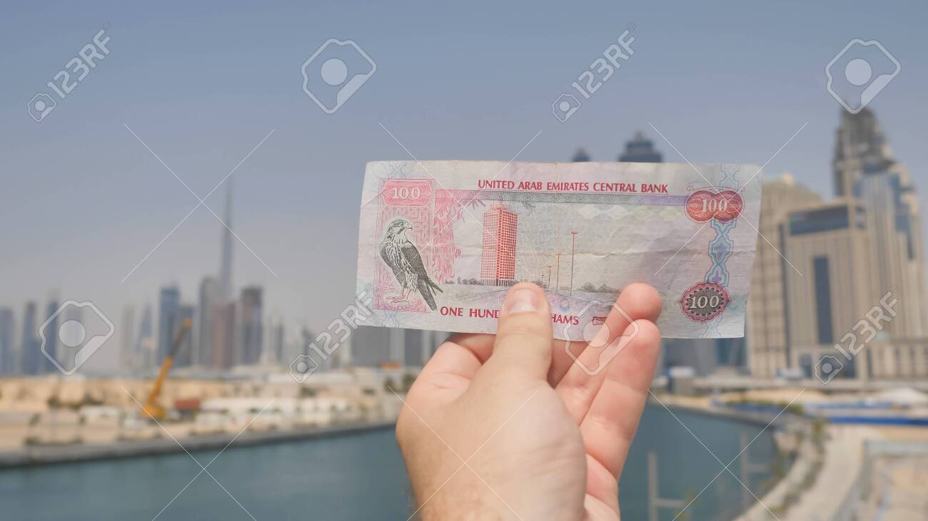男はドバイの街の手に100ディルハムの紙幣を保持しています。アラブ首長国連邦のお金。の写真素材・画像素材 Image 130351806