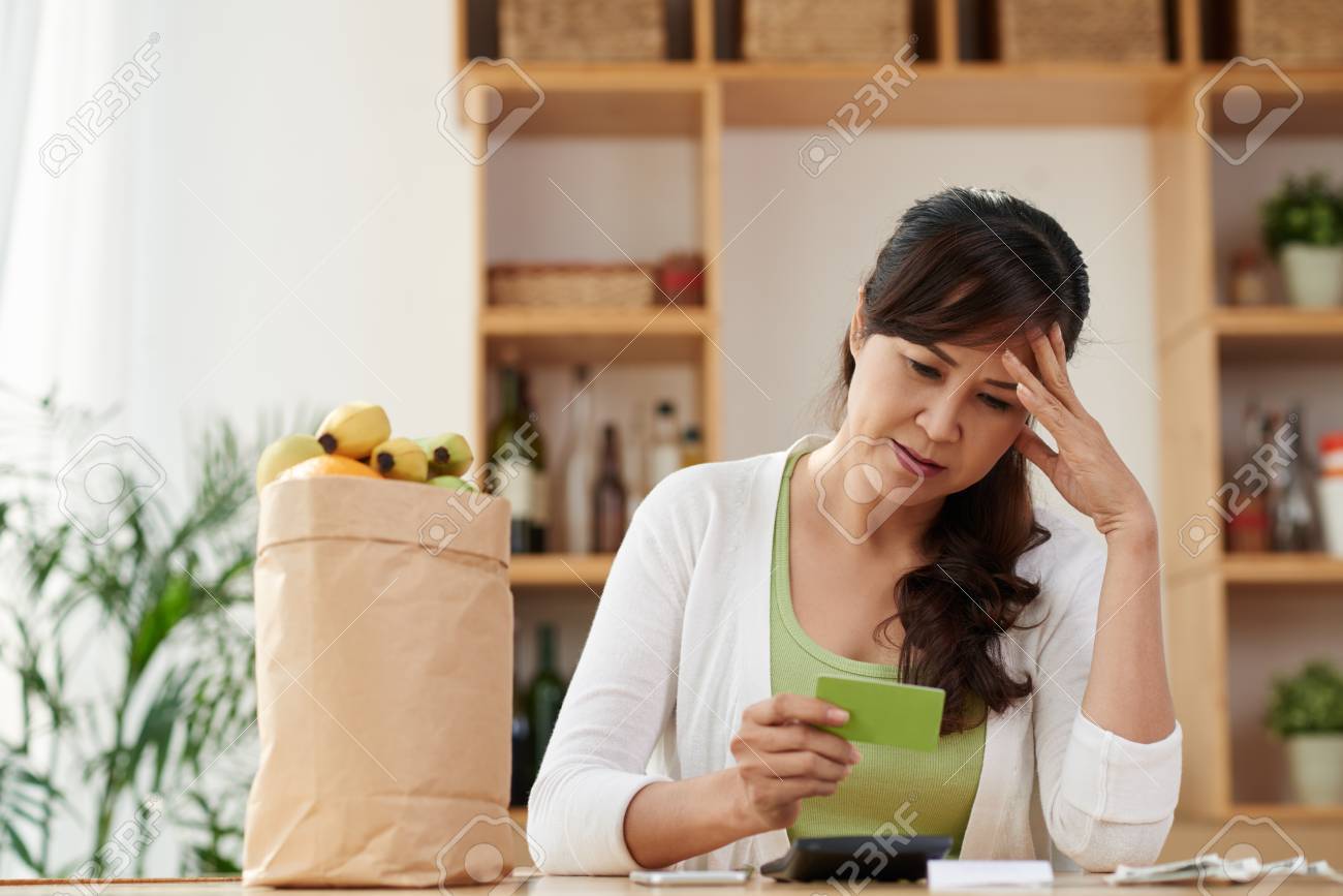 unhappy mature housewife looking at credit card after shopping stock