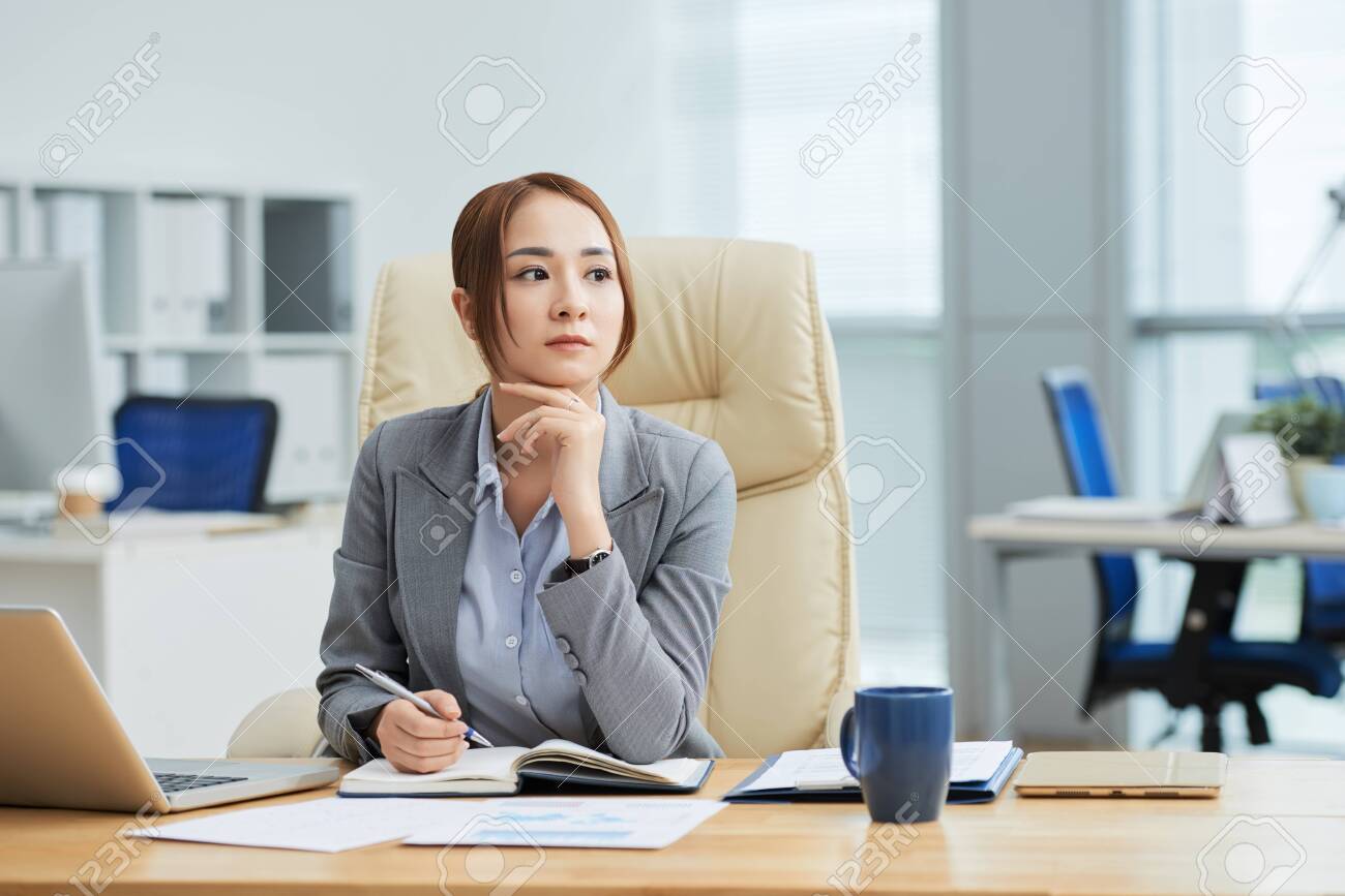 Serious Asian businesswoman sitting at her workplace with notepad and thinking over new business ideas at office - 123324598 Serious Asian businesswoman sitting at her workplace with notepad and thinking over new business ideas at office - 123324598