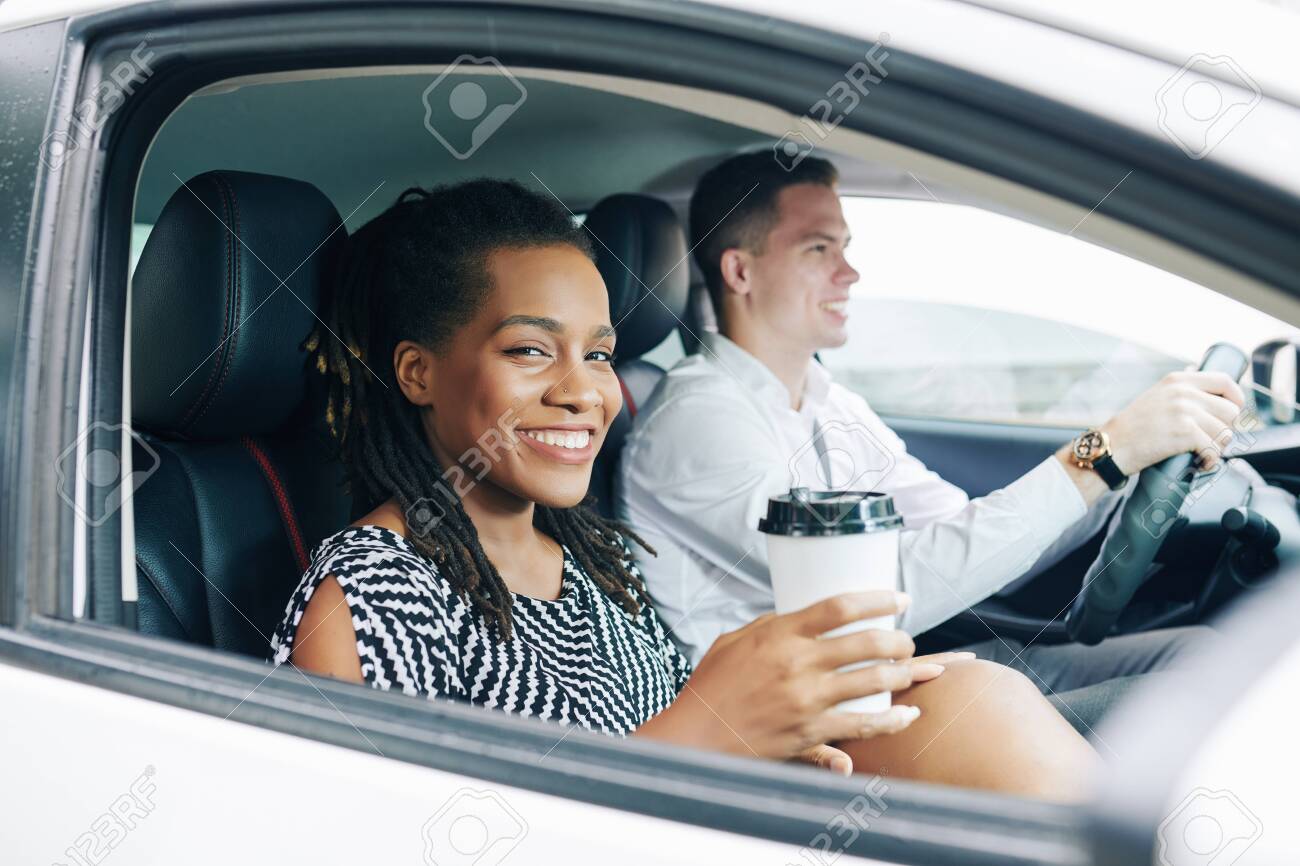 African young woman smiling at camera while drinking coffee during her trip by car together with young man - 130125349 African young woman smiling at camera while drinking coffee during her trip by car together with young man - 130125349