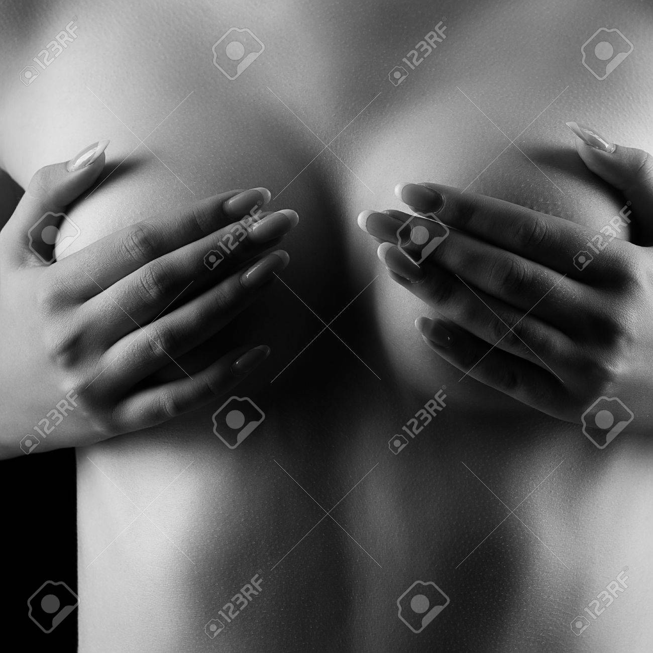 Stock photo woman covering her nude breast in studio photo with deep art shadows seduction and perfect body black and white image