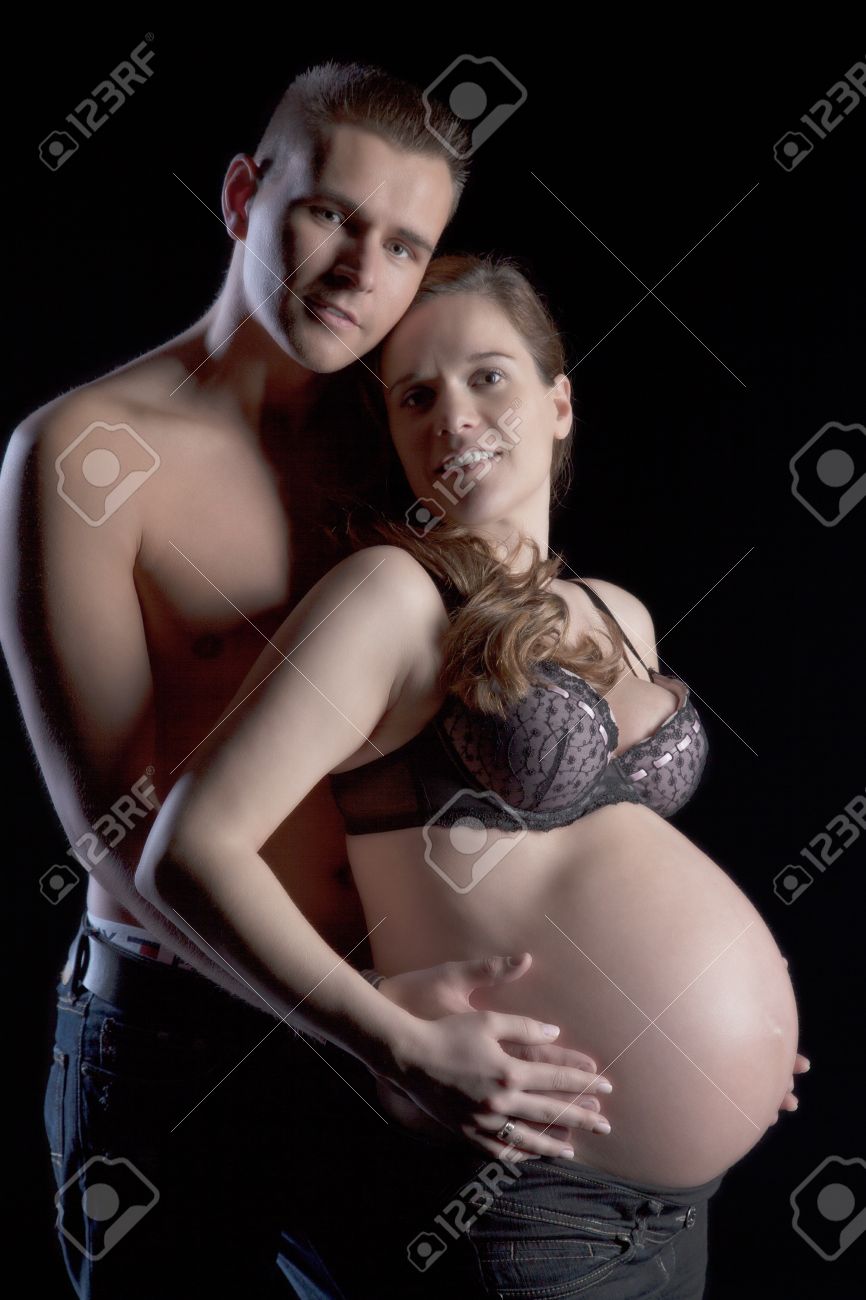 Young Man Holding Tenderly From Behind His Beautiful Pregnant Wife, On Black Background Stock Photo, Picture and Royalty Free Image