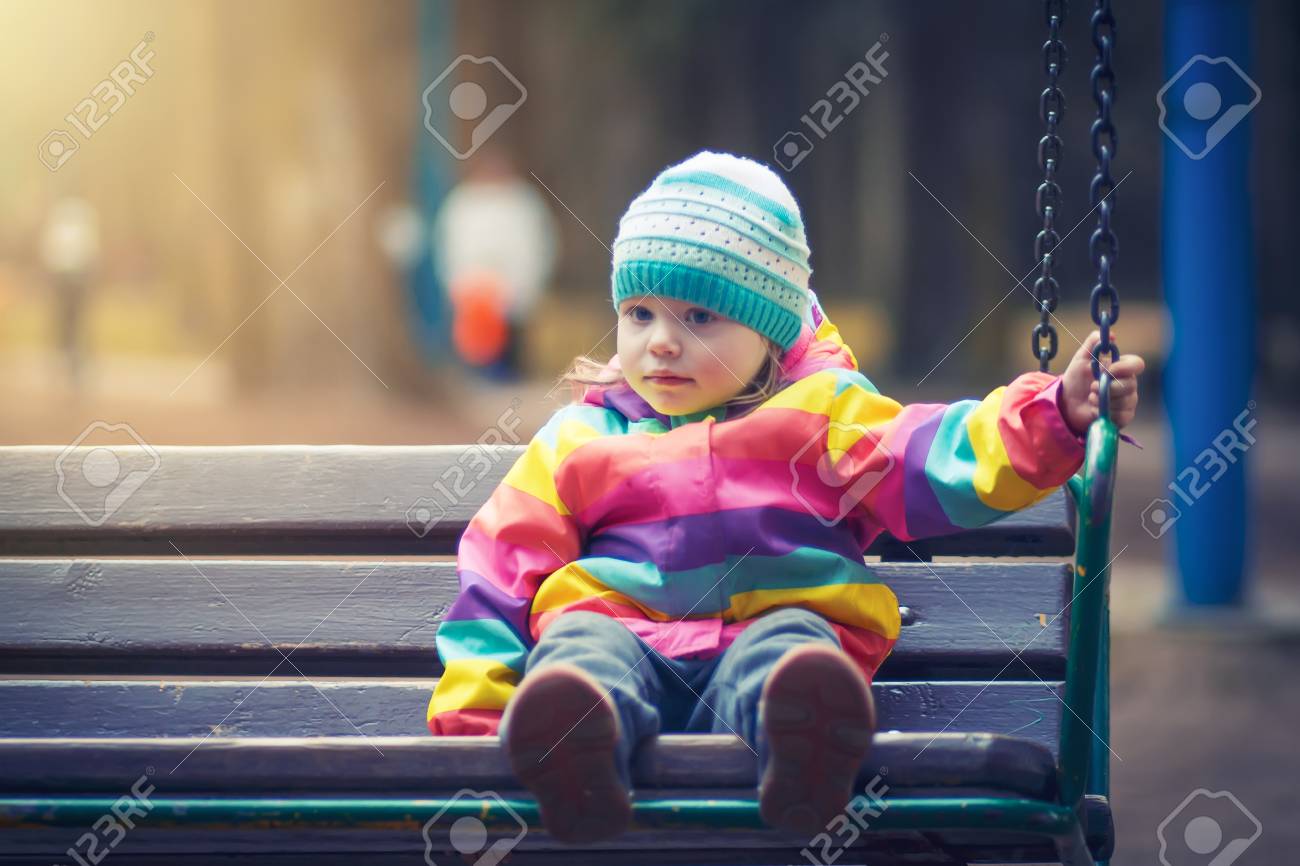 Little Girl Is Sitting On Swing In Evening Park Child Is Riding