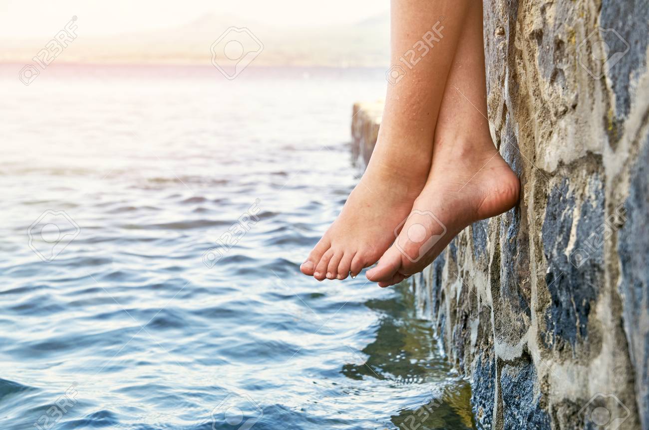 wet bare girl s feet dangling from the stone jetty stock photo