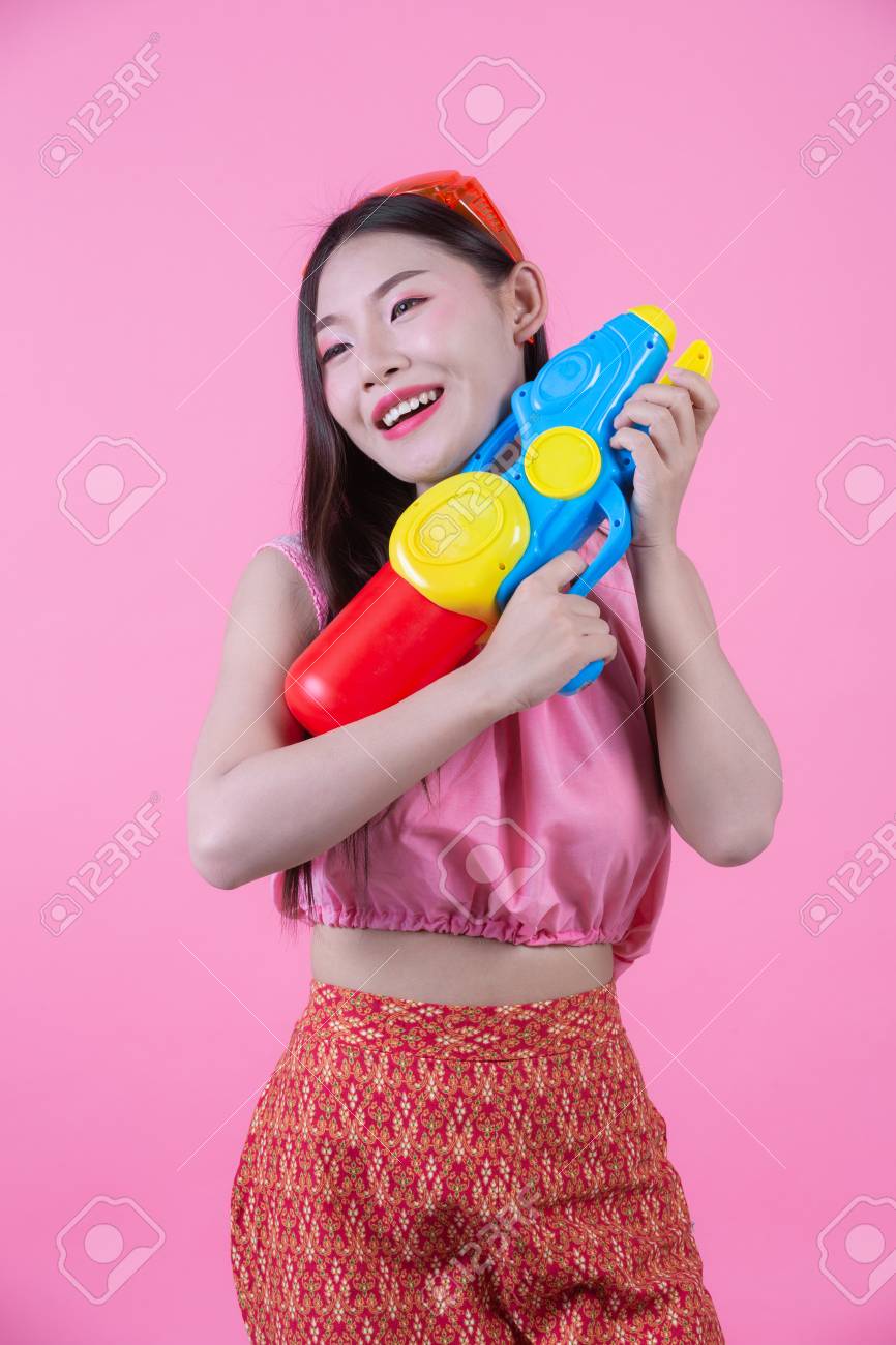 A woman dressed in a traditional Thai folk clothes holding a water gun on a pink background. - 120398354 A woman dressed in a traditional Thai folk clothes holding a water gun on a pink background. - 120398354