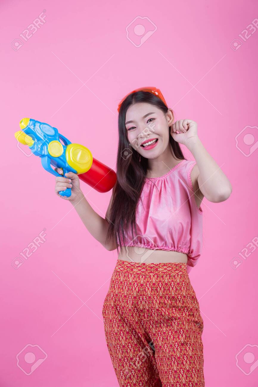 A woman dressed in a traditional Thai folk clothes holding a water gun on a pink background. - 120398357 A woman dressed in a traditional Thai folk clothes holding a water gun on a pink background. - 120398357