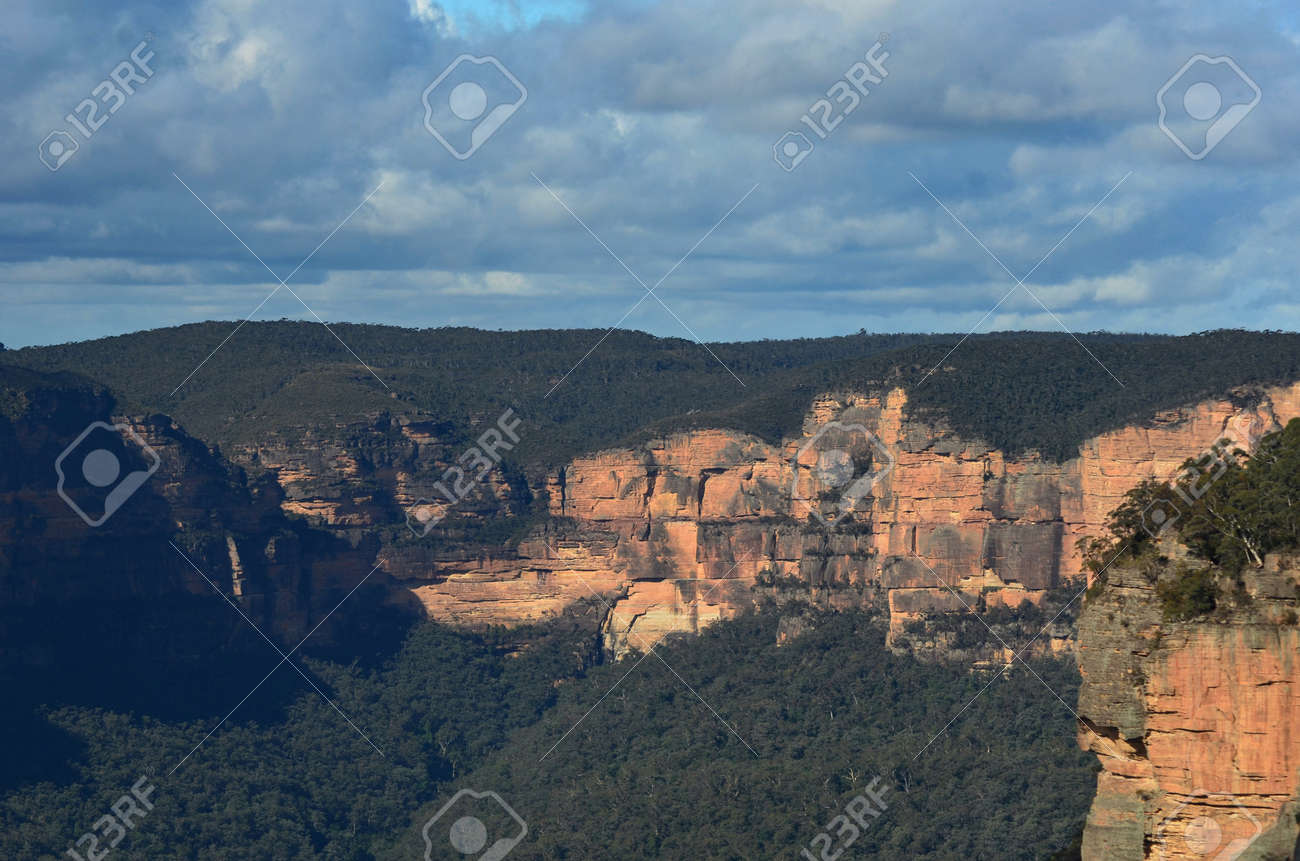 Sandstone cliffs are bathed in sunlight. They are surrounded by forest. The sky is overcast. They form part of the Megalong Valley in the Blue Mountains, Australia. - 152723795 Sandstone cliffs are bathed in sunlight. They are surrounded by forest. The sky is overcast. They form part of the Megalong Valley in the Blue Mountains, Australia. - 152723795