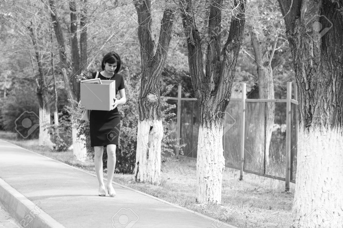 Upset brunette manager after being fired with a box of personal belongings is walking down the street. Black and white - 171374880 Upset brunette manager after being fired with a box of personal belongings is walking down the street. Black and white - 171374880