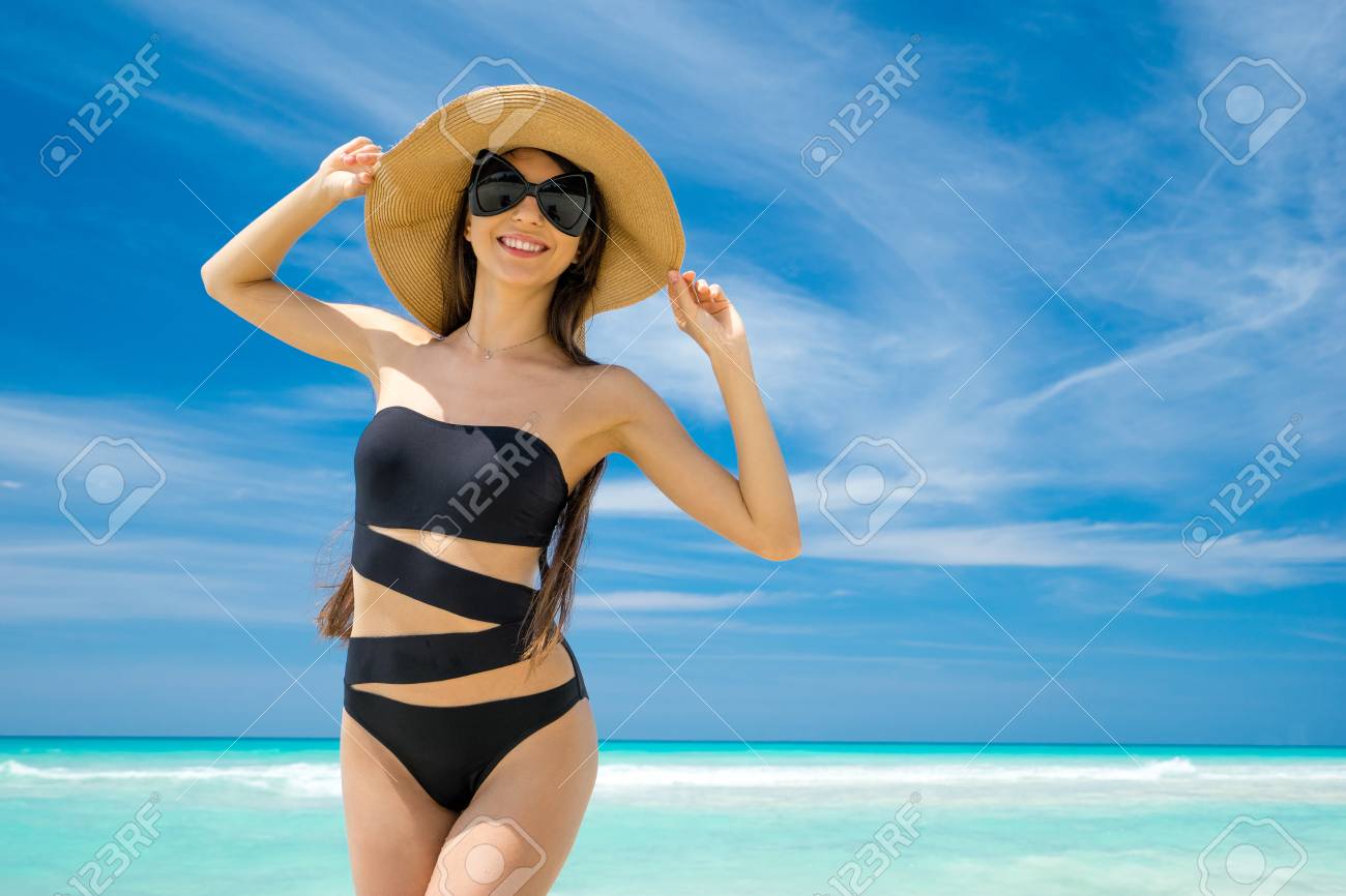 麦わら帽子 黒の水着とサングラスの美しい少女は笑顔と紺碧の海の背景にビーチに立っています 夏の暑い日 キューバの海岸 の写真素材 画像素材 Image
