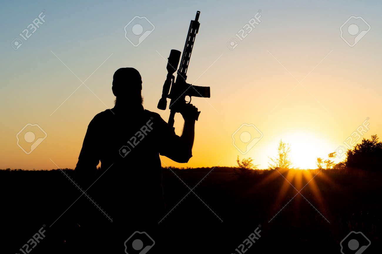 Silhouette of a man with a weapon in his hands on a sunset background - 155796847 Silhouette of a man with a weapon in his hands on a sunset background - 155796847