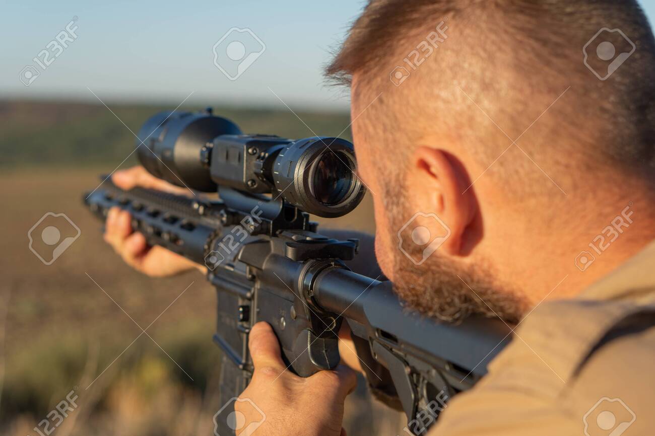A hunter with a weapon on the hunt against the backdrop of a beautiful summer landscape. Shooter sighting in the target. The Bearded man is on the hunt. Soft focus - 155640480 A hunter with a weapon on the hunt against the backdrop of a beautiful summer landscape. Shooter sighting in the target. The Bearded man is on the hunt. Soft focus - 155640480