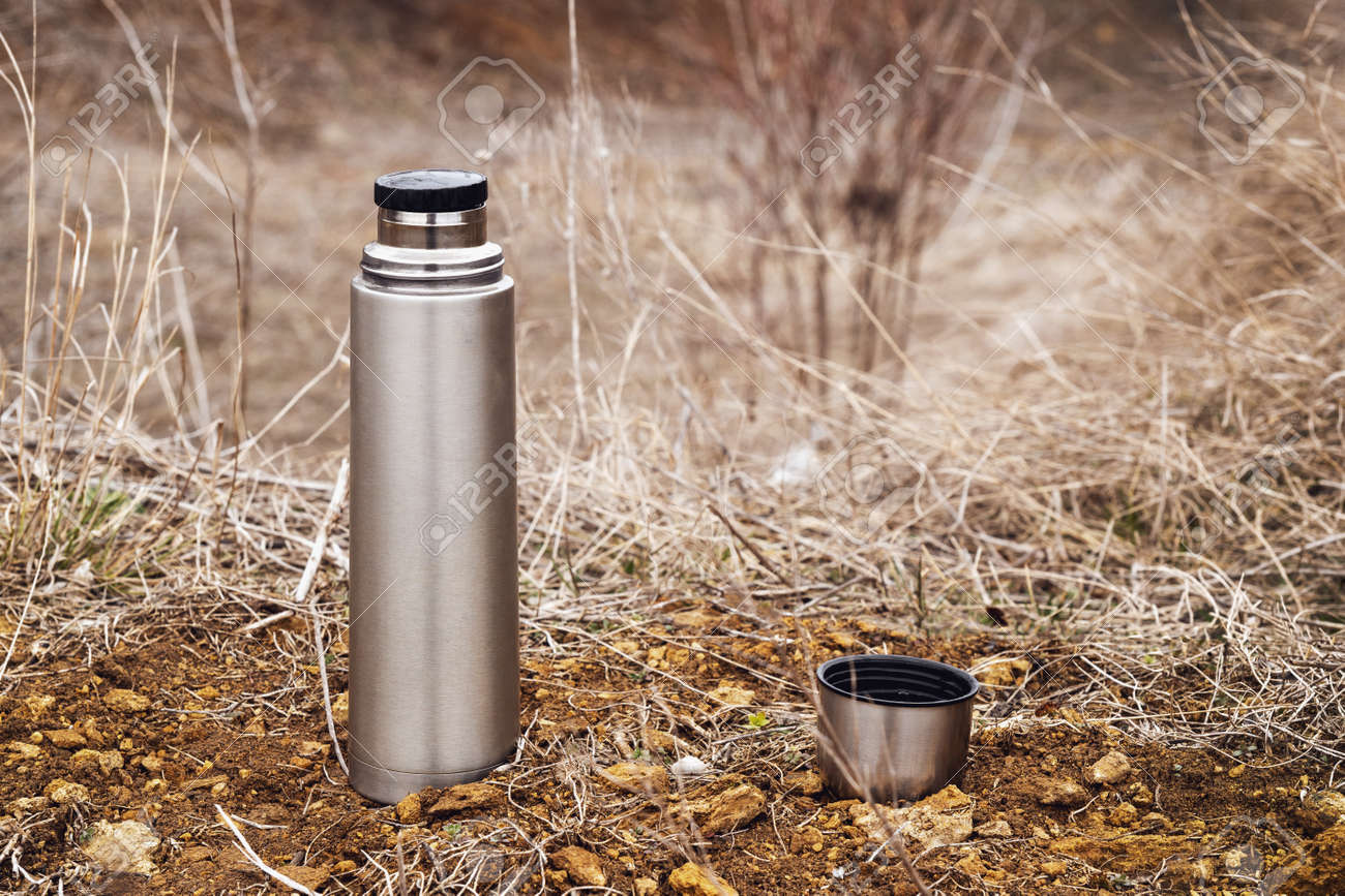 Steel vacuum flask with tea or coffee, outdoor. Hiking, active tourism, picnic, hot drink concept - 165799721 Steel vacuum flask with tea or coffee, outdoor. Hiking, active tourism, picnic, hot drink concept - 165799721