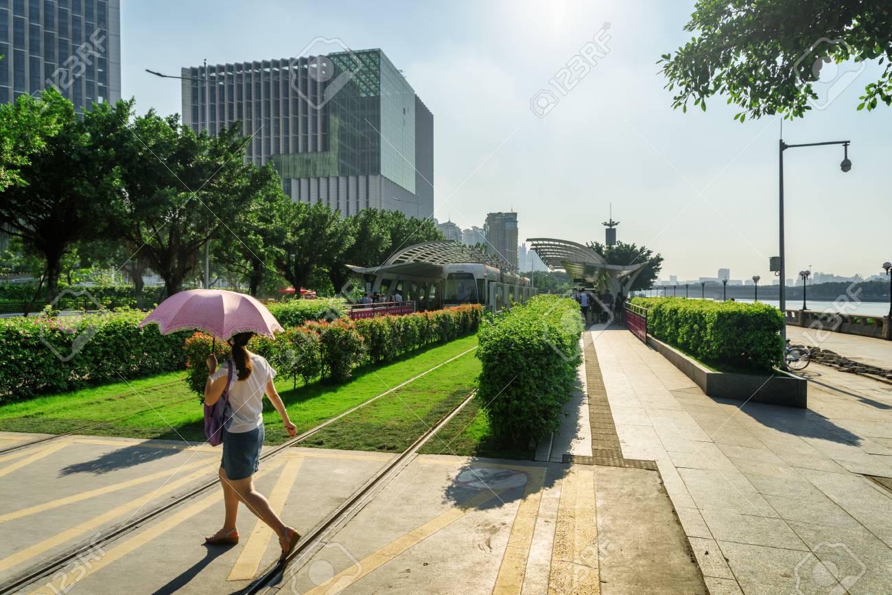 交差の傘でアジアの女性観光客は 中国広州市の中心市街地のトラムの停留所の近くにトラック芝生 トラムに搭乗がバック グラウンドで表示されます 広州 の路面電車システムは観光客に人気 の写真素材 画像素材 Image