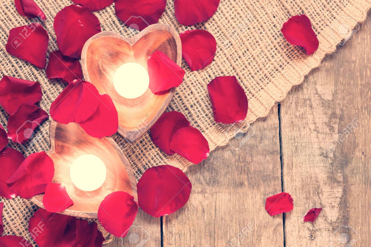 Enlightened Candles In Heart Shaped Candleholders With Red Roses Petals On Rustic Wooden Background Enlightened Candles In Heart Shaped Candleholders With Red Roses Petals On Rustic Wooden Background