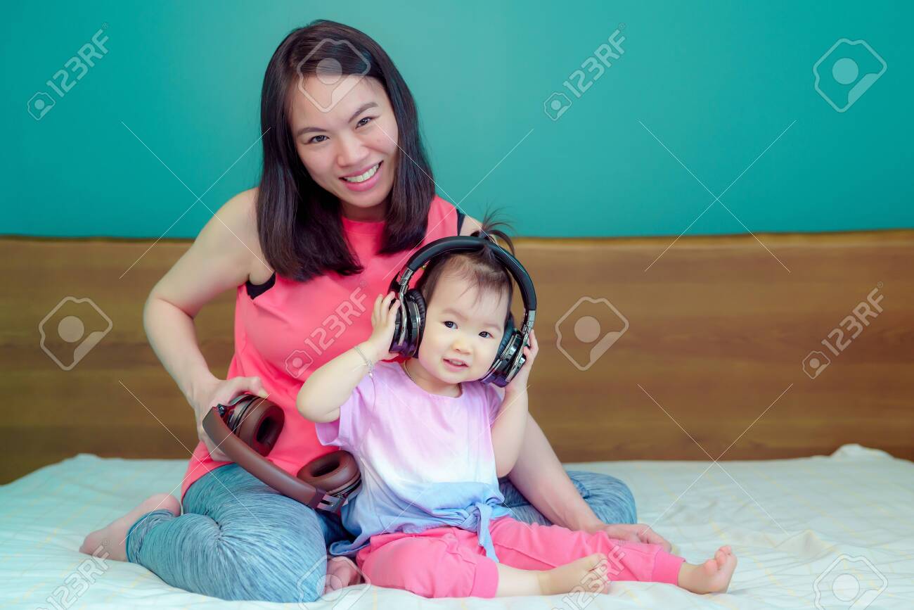 A beautiful Asian lady mother is pregnant. Take a big headset Come to the stomach Let the child in the belly listen Have a little daughter playing beside happily - 123616748 A beautiful Asian lady mother is pregnant. Take a big headset Come to the stomach Let the child in the belly listen Have a little daughter playing beside happily - 123616748