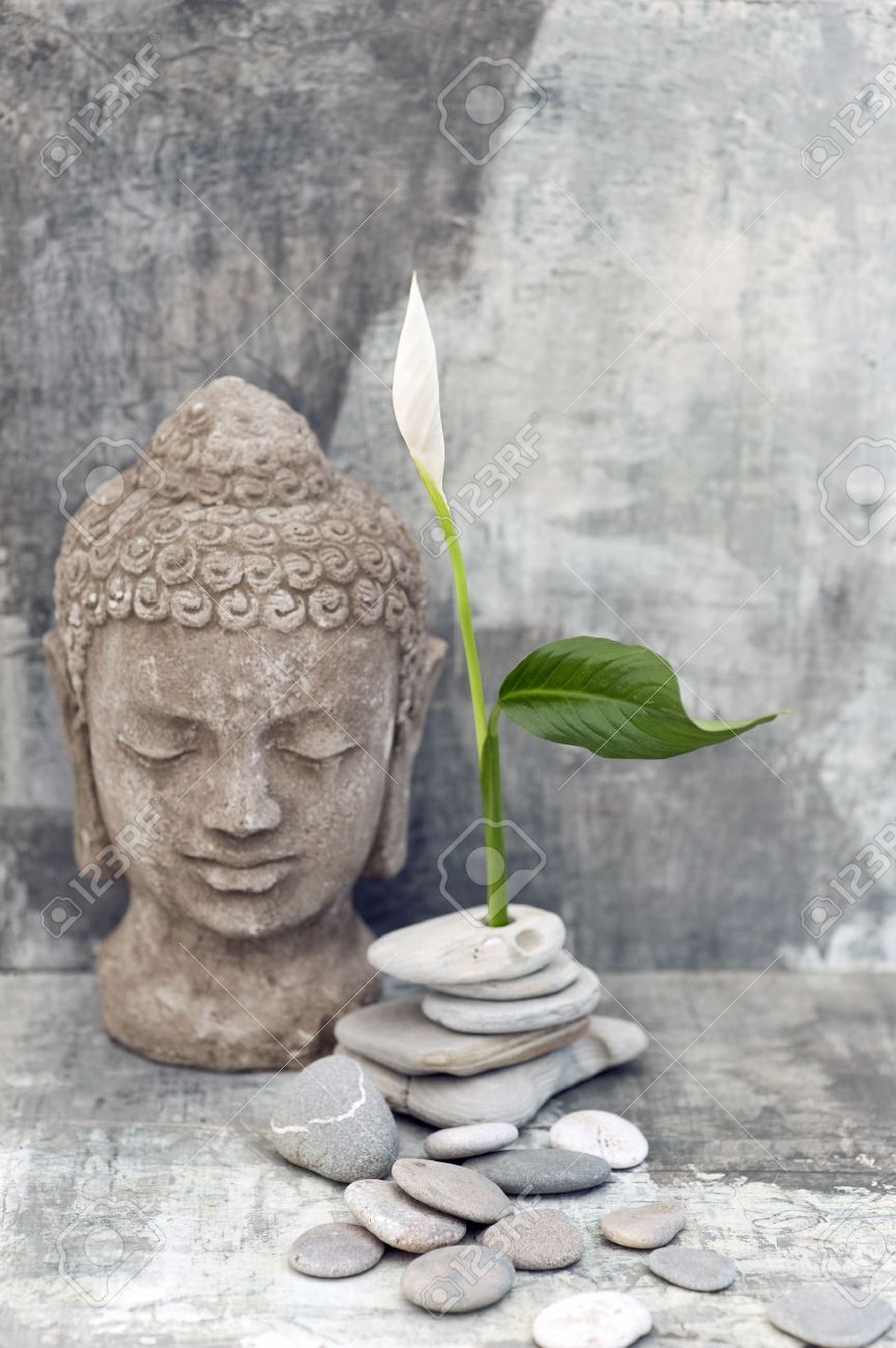 Stone Buddha head sculpture photographed with a white flower and stones - 15512579 Stone Buddha head sculpture photographed with a white flower and stones - 15512579