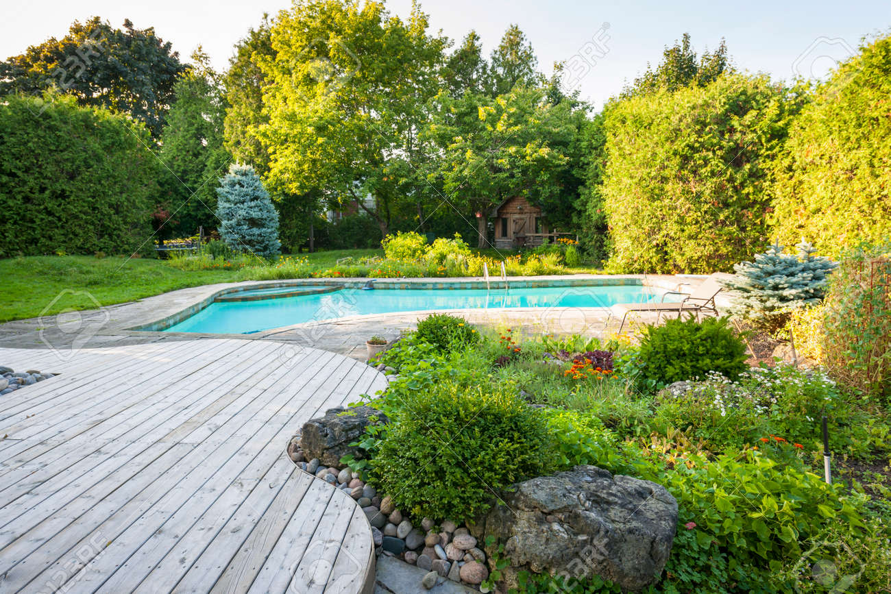 Backyard rock garden with outdoor inground residential swimming pool, curved wooden deck and stone patio - 33879226 Backyard rock garden with outdoor inground residential swimming pool, curved wooden deck and stone patio - 33879226